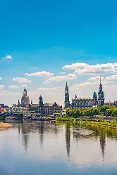 Panorama der Dresdner Altstadt mit Frauenkirche, Hofkirche und Residenzschloss, gespiegelt in der ruhigen Elbe unter blauem Himmel