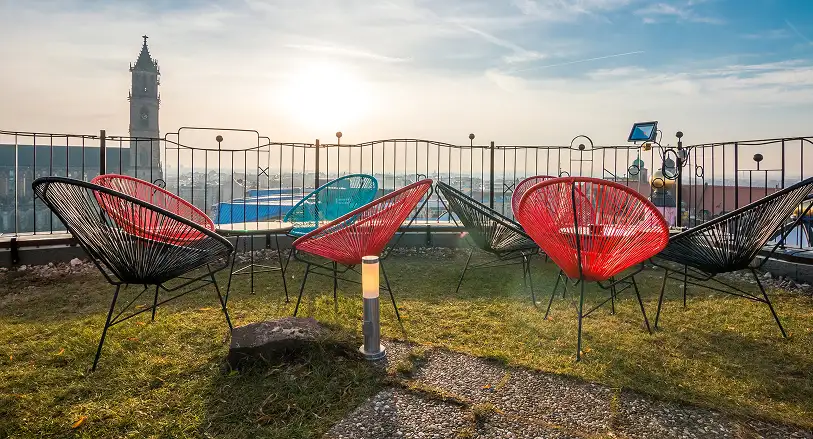 Rote und schwarze Designerstühle auf einer Dachterrasse mit Blick auf eine Stadt bei Sonnenuntergang, im Hintergrund ein hoher Kirchturm